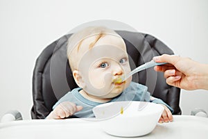 Baby in highchair eats cream soup with mothers help