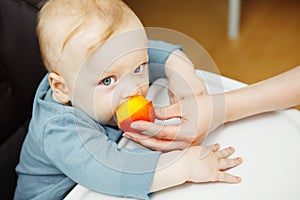 Baby in highchair and mother feeds him with peach