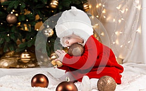 Baby hold christmas ball. A cute little girl in a red dress and white hat expresses emotions. Christmas concept with little kid,