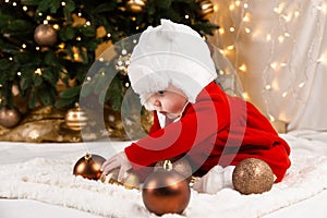 Baby hold christmas ball. A cute little girl in a red dress and white hat expresses emotions. Christmas concept with little kid,
