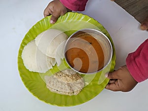 Baby Holding in Hand Home Made Indian vegetarian rice cakes breakfast known as idli or idly, served with sambar and Chatney in a