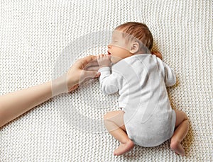 Baby holding Mother Hand. Sleeping Newborn lying down on Stomach. Beautiful Infant in Onesie sleep on White Blanket. Little Child