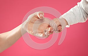 Baby holding mother`s finger on color background