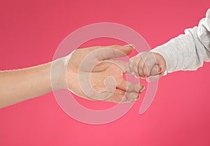 Baby holding mother`s finger on color background