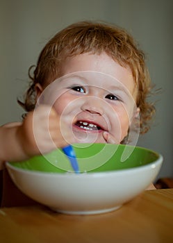 Baby holding a spoon in his mouth. Happy child eating himself with a spoon. Launching child eating food.