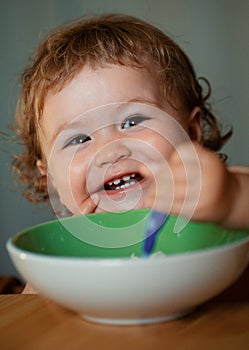 Baby holding a spoon in his mouth. Happy child eating himself with a spoon. Launching child eating food.