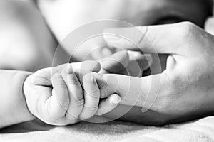 A baby is holding on to the mother& x27;s finger.Close-up.Black and white photo.Concept of motherhood and children& x27;s day