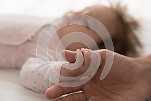 Baby holds fathers thumb in hand during carefree healthy sleep