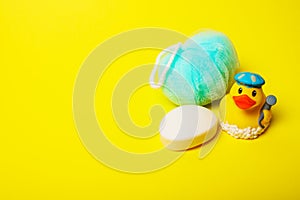 baby hygiene and bath items, baby soap, blue washcloth, yellow duck rubber toy on yellow background.