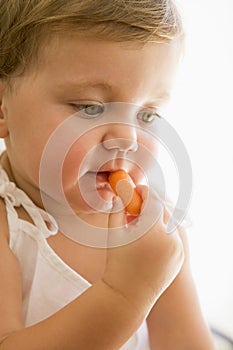 Baby indoors eating carrot.