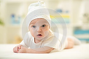 Baby lying on soft bed cover with cap