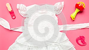 Baby items and clothing. Baby girl white dress. Flat lay composition. Child accessories, toy, clothers on pink background
