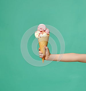 Baby kid hand holding big ice-cream in waffles cone on blue