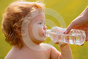 Baby kids drinking water from mother hands. Baby boy with curly blond hair drinking water in the park, holding plastic