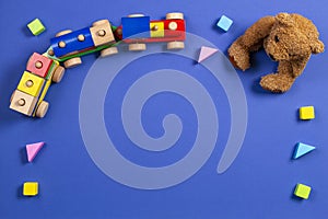 Baby kids toys background. Teddy bear, wooden train and colorful blocks on navy blue background