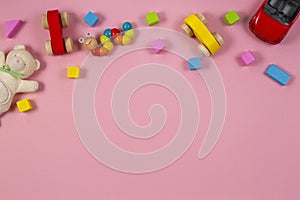 Baby kids toys frame with teddy bear, toy car, wooden train, colorful bricks on pink background. Top view