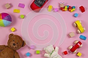 Baby kids toys frame with teddy bear, wooden toy car, colorful bricks on pink background. Top view
