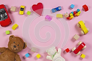 Baby kids toys frame with teddy bear, wooden toy car, colorful bricks on pink background. Top view