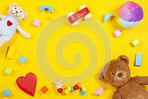 Baby kids toys frame with teddy bear, wooden toy car, colorful bricks on yellow background. Top view