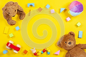 Baby kids toys frame with teddy bear, wooden toy car, colorful bricks on yellow background. Top view