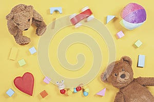 Baby kids toys frame with teddy bear, wooden toy car, colorful bricks on yellow background. Top view