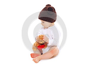 Baby in knitted brown hat with teddy bear toy sitting on white
