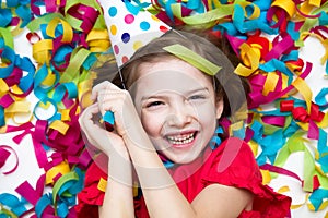 The baby lays in confetti on a white background. Celebrates a bright event, wearing a red dress and a hat.