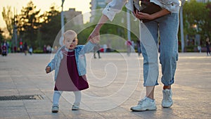 Baby learning to walk toddler taking first steps with mother helping infant teaching child at outdoor.