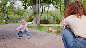 Baby learning to walk toddler taking first steps with mother helping infant teaching child at outdoor.