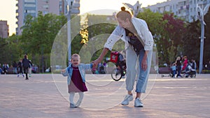 Baby learning to walk toddler taking first steps with mother helping infant teaching child at outdoor.