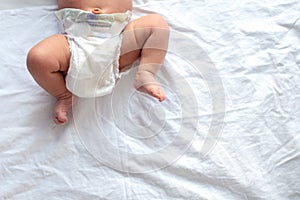 Baby legs and bottom in diaper on white bed background, top view, copy space