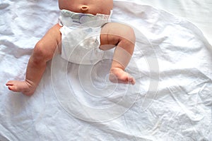 Baby legs and bottom in diaper on white bed background, top view, copy space
