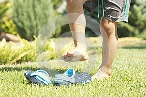 Baby legs and children`s blue slippers on the green grass in the garden, shoes for children, the concept of a healthy