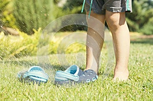 Baby legs and children`s blue slippers on the green grass in the garden, shoes for children, the concept of a healthy