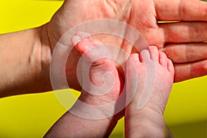 Baby legs on a yellow background, the mother holds the small legs of a newborn baby in her hand