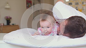 The baby lies on her stomach while supervised. . Happy father with toddler