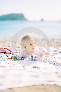 Baby lies on his stomach on the beach under the bright sun