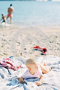 Baby lies on his stomach on a blanket on the beach