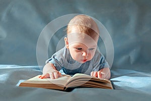 The baby lies on his stomach and reads an old book on a blue background