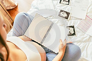 Baby list pregnant woman. Young pregnancy mother holding notepad. Pregnant lady writing check list of baby. Concept of