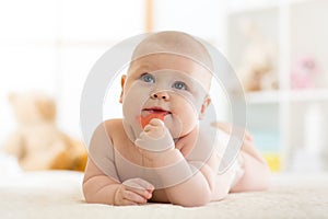 Baby little child bites teether lying on bed weared diaper