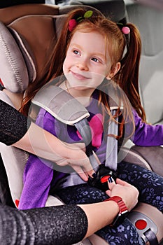 Baby little red-haired girl smiling while sitting in a child car seat.