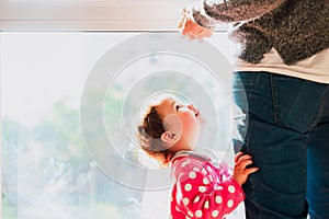 Baby looks at his mother hugging his legs, family domestic scene