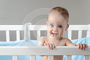 The baby looks with a trusting and kind look while standing in a crib