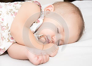 Baby lying on a bed while sleeping in a bright room