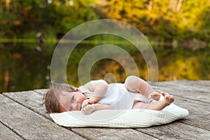 Baby lying on the blanket on pier hext to the river