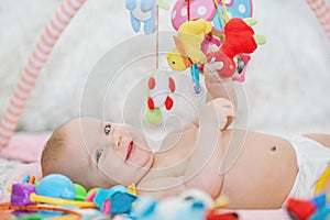 Baby lying on Developing rug. playing in Mobile. educational toys. Sweet child Crawling And Playing With Toys On Carpet