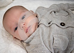 Baby lying with a grey sweater looks carefully