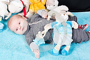 Baby lying on soft blue duvet Childhood and innocence concept Infant with blue eyes and peaceful smile among plush teddy bears