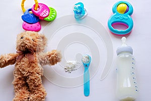 Baby milk powder, baby bottle and children`s toys on a light background flat lay